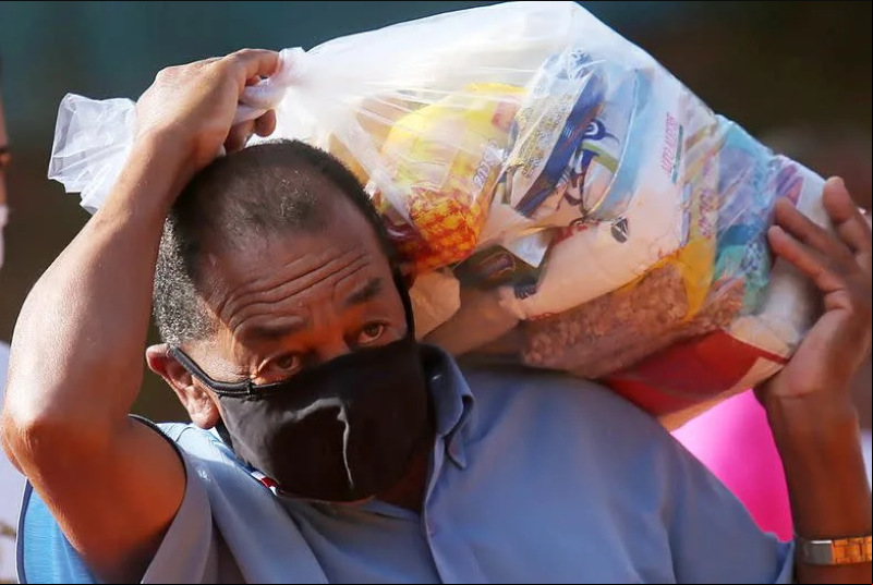 Morador de rua em SP carrega cesta básica distribuída durante a pandemia da COVID-19